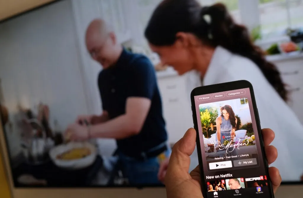 A phone shows Netflix’s Meghan Markle series while a TV plays footage of the show — a reminder of the commercial path the couple chose after leaving Britain.